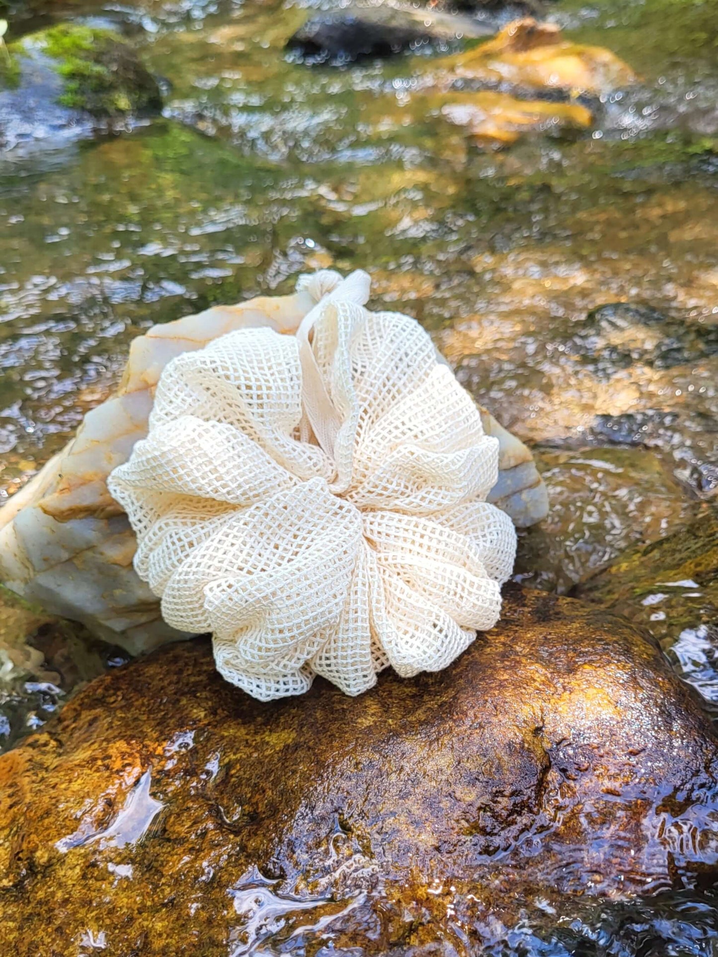 Organic cotton shower pouf in front of a creek