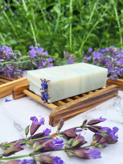 Raccoon lard soap on a natural bamboo soap dish with blue cornflower petals and fresh sage blossoms